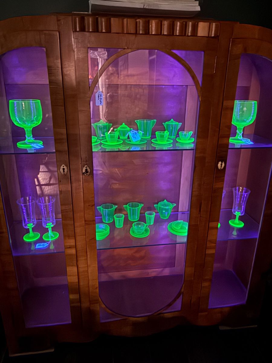 Akro agate child’s tea set and other uranium glass in an art deco backlight cabinet