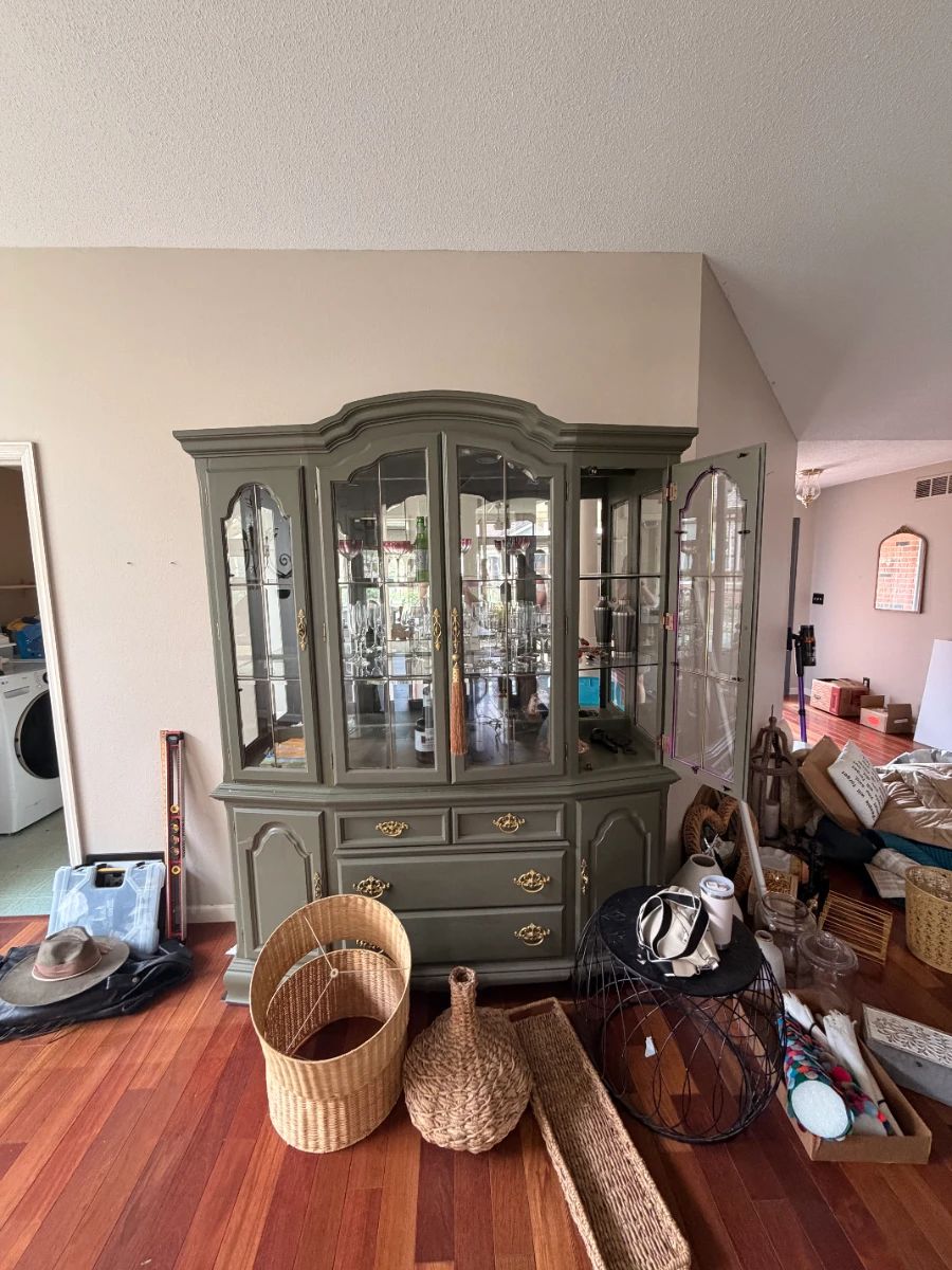 A stately hutch in a sophisticated sage green finish, featuring glass display doors, brass hardware, and ample storage below.
