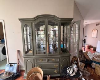 A stately hutch in a sophisticated sage green finish, featuring glass display doors, brass hardware, and ample storage below.