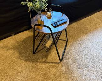 industrial round end table featuring a wood-look top and a V-shaped black metal magazine rack