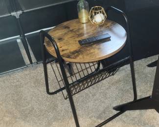  round industrial side table featuring a rustic wood top and a black metal magazine rack