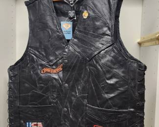 black leather motorcycle vest with side lacing, featuring multiple patches including a USA flag and a "Freedom Ain't Free" emblem.