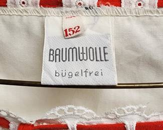 Clothing label reading "Baumwolle bügelfrei," indicating that the garment is made from cotton and is non-iron. The label also displays a size 152 and a red fabric tag, suggesting it is part of a vintage or retro-style outfit.