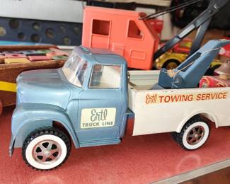  Vintage ERTL Towing Service toy truck with a blue cab and white trailer, displayed among other classic children's toys. The ERTL brand, known for its pressed steel vehicles