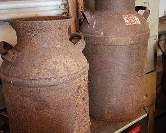 Two large, rusted vintage milk cans with handles and lidded tops