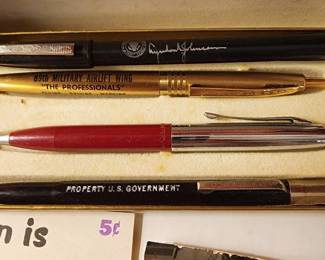 Gold-colored pen marked with the U.S. Military Airlift Wing insignia and a red and silver ballpoint pen.