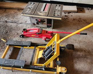Hein-Werner hydraulic floor jack alongside a red Harbor Freight motorcycle lift jack and a table saw