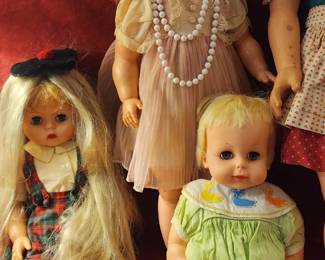 group of vintage dolls, including a Shirley Temple doll in a pastel dress with a pearl necklace, alongside other collectible figures