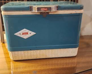 Vintage Coleman blue and white metal cooler with a diamond-shaped logo on the front
