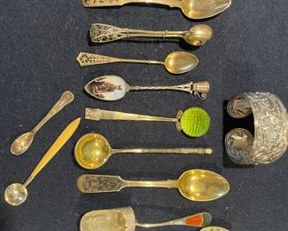 A rare assortment of gold-washed and sterling collector spoons, featuring vibrant plique-à-jour enamel, hand-painted scenics, and a stunning heavy floral repoussé cuff bracelet