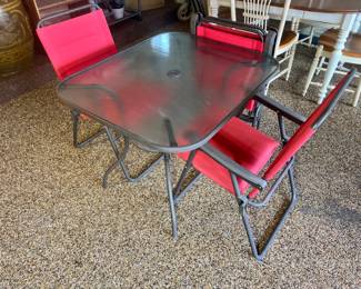 Outdoor bistro set featuring a square glass-top table and red mesh folding chairs