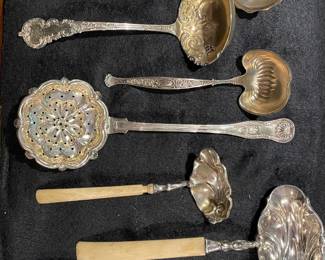 An exquisite collection of ornate sterling silver serving ladles and a large pierced sifter spoon, some featuring elegant bone handles