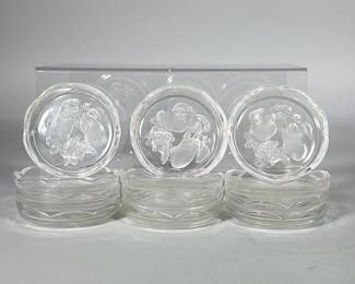 (12pc) VAL SAINT-LAMBERT STYLE CRYSTAL COASTERS, ETCHED FRUIT MOTIF | Set of twelve clear pressed crystal coasters, each with a scalloped rim and a central frosted/etched fruit motif depicting pears and a grape cluster. Low circular profile with molded rim details and visible mold seams consistent with pressed production. Undersides smooth with no visible maker's mark.