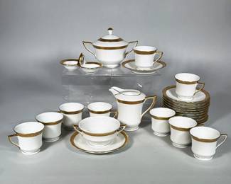 (25pc) GLORIA (CZECHOSLOVAKIA) PORCELAIN DEMITASSE SET | White porcelain demitasse service with gilt ornamental band and gold-accented handles. Comprising 10 demitasse cups, 11 saucers, one teacup with attached saucer, covered sugar bowl, creamer, and double-open salt cellar as reported in inspection. Backstamp in green with a shield reading "GLORIA" and marked "Czechoslovakia" with additional script indicating hand-applied decoration. Design details include a narrow gilt rim at the foot and a patterned gilt border around cup rims and saucer edges.