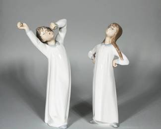 (2pc) LLADRÓ PAIR OF PORCELAIN CHILD FIGURINES, BOY AND GIRL | Pair of glazed Lladró porcelain figures depicting children in long nightgowns; one boy stretching with arms raised and one girl standing with hands on hips. Both figures have white bodies with pale blue collars, painted facial features, and naturalistic hair coloring on the heads. Glossy glaze overall with subtle modeling of drapery on the gowns. 