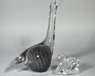 (2pc) SIGNED MURANO-STYLE ART GLASS SWAN WITH CUT CRYSTAL SWAN FIGURINE | Larger signed Murano-style art glass swan with an elongated clear neck and a rounded body containing a grey filigree/reticello pattern with numerous small internal air bubbles. Smaller faceted cut crystal swan with a curved neck and multi-faceted body that produces noticeable prismatic dispersion. Both pieces are free-standing and finished with smooth, polished rims and bases. The larger piece is signed.