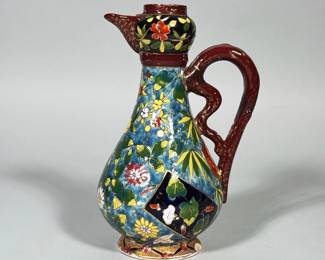 FISCHER BUDAPEST HAND-PAINTED ENAMELED EWER | Pear-shaped earthenware ewer with an applied sinuous red handle and short spout. Body decorated in polychrome enamels on a blue ground with gilt outline highlights forming floral sprays and dark blue cartouche panels; foot with a gilt band and small flower motif. Underside stamped "FISCHER BUDAPEST PATENT." Dimensions: h. 7.5 x dia. 2.75 in (dia. of base)