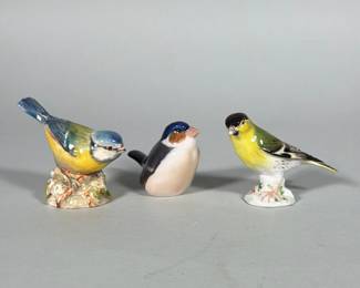 (3pc) GROUP OF THREE PORCELAIN BIRD FIGURES INCLUDING ROYAL WORCESTER AND MEISSEN-MARKED | Group of three small polychrome porcelain bird figurines, each hand-painted and glazed. One piece bears a purple printed mark reading "BLUETTI BONE CHINA ROYAL WORCESTER MADE IN ENGLAND" on the base; a second has a blue crossed-swords mark on the underside; the third has painted numerals ("1040" and additional blue painted marks) on the base. Two birds are modeled on small naturalistic floral bases; the third is a smoother, simplified form with a glossy finish. Surfaces are glazed with detailed painted plumage in yellow, blue, black and brown tones.