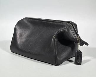 COACH BLACK LEATHER ZIP TOILETRY BAG / DOPP KIT | Black leather rectangular toiletry bag with top zip closure and dual leather zipper pulls. Features a leather Coach hang tag on a ball chain and a small embossed Coach stamp on the exterior side. Interior is fabric-lined with a zippered pocket along one wall; silver-tone hardware throughout. Boxy Dopp kit silhouette with piped leather corners.