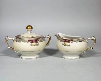 (2pc) MEITO CHINA PORCELAIN CREAMER AND COVERED SUGAR BOWL | Porcelain creamer and covered sugar bowl with cream-colored ground, transfer-printed and hand-applied magenta enamel and gilt decoration. Sugar bowl has a domed lid with a gilt ball finial; both pieces are raised on circular footed bases. Molded double handles are finished with heavy gilt accents. Decoration includes a narrow foliate/scroll band around the rim and small gilt floral sprays on the body.