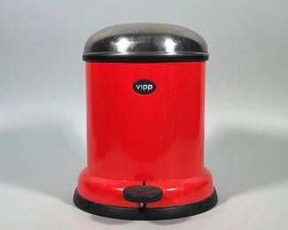 VIPP (DENMARK) RED MINI PEDAL BIN WITH STAINLESS DOME LID | Red cylindrical metal pedal bin by Vipp with a domed stainless-steel lid and a black rubber trim. Sits on a black rubber base with a round foot pedal and inset oval black-and-white "vipp" badge on the front. Pedal-operated hinge assembly at the base with a visible slot for the pedal linkage. Construction appears to be painted/coated steel for the body with metal lid and rubberized base.