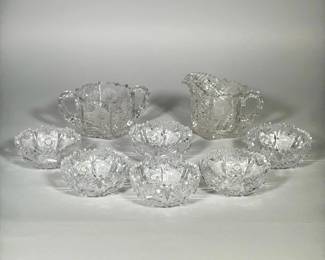 (8pc) AMERICAN BRILLIANT-STYLE CUT GLASS CREAMER, SUGAR & NAPPIES | Cream-ground porcelain urn with twin ornate gilt handles, narrow neck and molded ribbed sides. Front and back feature an oval polychrome enameled floral panel outlined in raised gold; additional raised gilt scrollwork at the foot and neck. Underside shows a drilled hole through the base and a blue painted script mark. Decoration appears applied with raised gilt outlines and hand-painted enamels in pink, purple and green tones.