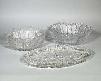 (3pc) BRILLIANT CUT GLASS SERVING LOT | Three-piece lot of clear cut glass comprising two scalloped round bowls and an elongated scalloped oval tray. Deep wheel-cut decoration includes starburst centers, hobstar motifs, fan and cross-hatched panels with pronounced faceting. Rims are scalloped/zigzag and the pieces display repeated geometric panels around the body. All pieces are clear glass with heavy, high-relief cutting visible on exterior and interior surfaces.