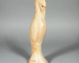 CARVED ONYX EGRET FIGURINE | Polished banded stone carved in a stylized egret form mounted on a flared pedestal base. Pale peach, cream and orange veining throughout with a polished translucent agate-like cavity exposed on one flank. Small dark inlaid eyes set into a tapered head; overall surface is smooth and highly polished. Carving emphasizes simplified wing and tail planes with minimal incised detail. Dimensions: h. 8 x w. 2.5 x d. 1.75 in
