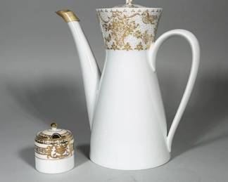 (2pc) ROSENTHAL (BJORN WIINBLAD) PORCELAIN COFFEE POT & NORITAKE HANDPAINTED PORCELAIN SUGAR BOWL | Two-piece lot: a Rosenthal Studio Linie porcelain coffee pot decorated with a gilt floral/garland band at the neck, tall conical body, long curved spout with gilt tip, and loop handle; underside bears the Rosenthal Germany mark, Bjorn Wiinblad signature and Studio Linie label. Accompanying Noritake lidded sugar bowl in white porcelain with matching gilt band, spoon notch in lid and gilt finial; underside bears a red Noritake "M" wreath mark with "HANDPAINTED MADE IN JAPAN" and number No.37532. Both pieces are white porcelain with applied gold decoration and visible factory/artist marks on the bases.