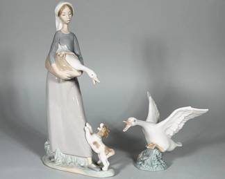 (2pc) LLADRÓ (SPAIN) GIRL WITH DOG AND GEESE PORCELAIN FIGURES | Two polychrome glazed porcelain figures: a standing young woman in a long dress holding a goose with a small dog at her skirt on an oval ground, and a separate winged goose mounted on a small mound base. Soft pastel palette of grays, beige and white with glossy finish and modeled details in the wings, basket and dog. Blue LLADRÓ backstamp reading "LLADRÓ HAND MADE IN SPAIN" and an additional "DAISA" mark are visible on the bases; several impressed model/puzzle numbers are also present. Both pieces have factory vent holes visible on the undersides.
