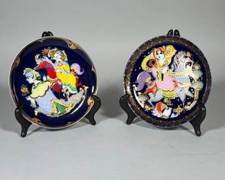 PARIAN BISQUE FIGURAL SCULPTURE OF SEATED WOMAN | Two Rosenthal Studio-Line porcelain collector plates designed by Bjørn Wiinblad, titled "Aladin und die Wunderlampe IX" and "Zauberpferd III" as marked on the versos. Deep cobalt-blue ground with polychrome enamel decoration and gold gilded accents; both faces signed "B. Wiinblad" in the design and backstamped "Rosenthal studio-line GERMANY" with series wording. Each plate displays a central figural scene of riders and horses rendered in Wiinblad's stylized palette and line work.