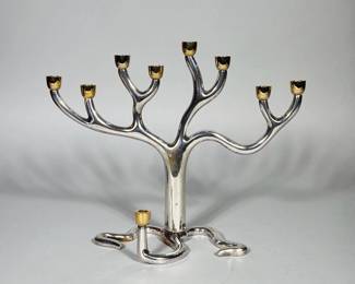 SANDRA KRAVITZ FOR ROSENTHAL SCULPTURAL MENORAH | Cast, polished silver-tone metal menorah with an organic, tree-like form featuring seven upward branching arms and one lower arm; each cup is finished in a gold-tone (gilt) metal. Sinuous three-legged base integrates a secondary low candle arm. Includes a fitted red velvet presentation box with red satin lining printed “SANDRA KRAVITZ ORIGINAL Presented by THE ROSENTHAL JUDAICA COLLECTION.” Design is modern/contemporary in approach with smooth, rounded branches and integrated construction.