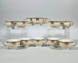 (12pc) NORITAKE / MEITO CHINA SAVONA IVORY PORCELAIN TEACUPS | Group of twelve porcelain teacups with an ivory ground, gilt rims and ornate gilt-accented scroll handles. Each cup features a magenta cartouche with gilt floral and foliate ornament around the upper band and a single gilt line encircling the body above the foot. Underside backstamp reads "EMPIRE SHAPE MEITO CHINA SAVONA" and is additionally marked "Ivory China." Cups are footed with a slightly flared rim and applied loop handles with decorative detailing. Dimensions: 