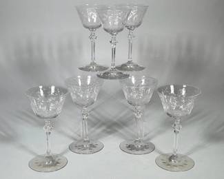 (7pc) CUT GLASS STEMWARE WITH FLORAL ETCHING | Set of six clear cut glass stemware with shallow, flared bowls decorated with engraved floral and leaf motifs. Each glass has a long, slender stem with a faceted knop and a flat circular foot featuring a ring of punched circular depressions. The bowls display starburst-style cuts and fine linear engraving. 