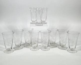 (11pc) Etched Glass Tumblers With Starburst Motif | Set of eleven clear, conical footed tumblers decorated with engraved/etched starburst motifs and smaller incised stars scattered above the main motif. Each glass features a slightly flared rim, a conical bowl that tapers to a short stem, and a round flat foot. Etching appears as linear, radiating cuts forming a central starburst on the bowl of each tumbler. Bases and stems are plain clear glass.