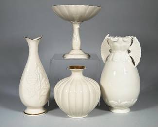 (4pc) LENOX IVORY-GROUND PORCELAIN VASES AND PEDESTAL COMPOTE | Group of four ivory-glazed porcelain pieces by Lenox comprising a fluted pedestal compote, a ribbed globular bud vase with gilt interior rim, a tall teardrop bud vase with applied floral relief and gilt trim at rim and foot, and an urn-form vase with fan-like applied handles. All pieces are glazed in a uniform creamy ivory tone with gold accenting on rims and bases. The underside of one vase is stamped with a gold Lenox wreath mark and the words "Lenox Made in U.S.A.". Forms include fluting, applied relief floral decoration, and decorative openwork handles. Dimensions: h. 7.25 x dia. 2.5 in (dia. at opening)