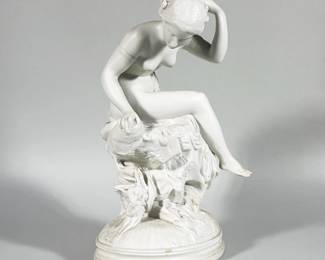 PARIAN BISQUE FIGURAL SCULPTURE OF SEATED WOMAN | Unglazed white bisque (Parian-style) figural sculpture depicting a semi-nude seated woman arranging her hair, raised on an oval stepped base. The composition includes a draped rock and floral motifs integrated into the base. Surface appears matte with fine modeled detail in the hair, hands and drapery folds.