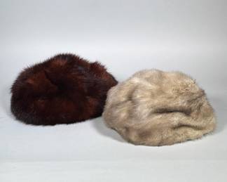 (2pc) PAIR OF VINTAGE FUR PILLBOX HATS | Pair of round pillbox-style fur hats, one dark brown and one light gray-beige. Each hat has a diameter of 9 in. and a low, rounded crown with a brimless profile. The dark brown hat shows a visible black fabric lining at the interior opening. Constructed from short, dense fur pelts with natural guard-hair highlights.