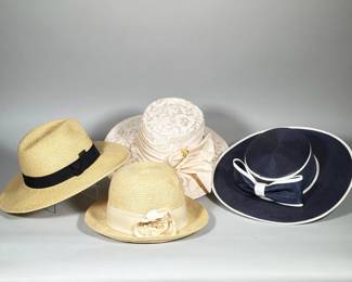 (4pc) GROUP OF SUN HATS | Group of four sun hats comprised of braided straw and fabric constructions, including a lace-covered blush round crown hat, two natural-tone straw hats with ribbon bands and a navy wide-brim straw hat with white trim and bow. One natural straw hat features a black grosgrain band with a small metal maker plaque reading "Sun N Sand." Interior label reads "Sun N Sand Headwear EST. 1986" and shows a website address. 