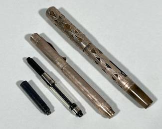 PAIR OF VINTAGE WATERMAN FOUNTAIN PENS WITH INK CARTRIDGES | Pair of vintage fountain pens shown with two ink cartridges/convertor units. One pen features a pierced sterling overlay revealing a brown/amber celluloid barrel and a clip stamped "WATERMAN'S," with cap band stamped "STERLING" and "MADE IN U.S.A." The second pen has a knurled metal body and shows a "925" mark on the cap band. Height: 5.25 in. Dimensions: 