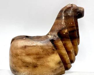 This Pre-Columbian Inca hand-carved stone animal figure offers a minimalist, stylized view of a llama or alpaca conopa or canopa in votive vessel form. These figures are ritual objects used as containers for offerings to Inca gods, typically held in a small hollow in the back. They were often buried in pasture land to increase llama herds or offered to Pachamama, Mother Earth. As is typical of these animal sculptures, this one was carved from stone with natural color variations, and is characterized by a simplified, stylized form. These objects originate from the Andes region, particularly around Cusco, Peru, and date back to the 15th-16th century.