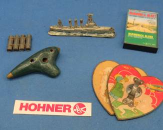 Lot 109. Harmonica stew: 5 1/2" heavy (non-magnetic) toy SMS Emden. This ship was the scourge of the Allied navies capturing or sinking 21 vessels before being driven aground by the HMAS Sydney in 1914. Broken valentine accordion. Clay ocarina. Harmonica cassette tape and more.
