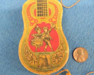 Lot 155. Vintage German toy 7" paper guitar with a lithograph printing of a boy and a girl dancing and an attached 8-hole harmonica with poor sound