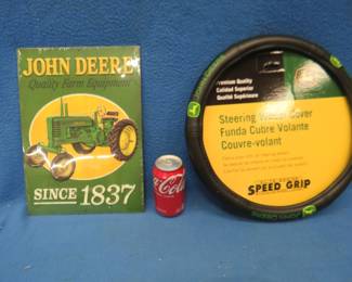 Lot 261. Two brand new John Deere items. A 14" x 10" metal sign and a John Deere steering wheel cover.