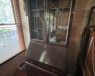 A dark wood secretary bookcase with leaded glass doors and ball-and-claw feet.