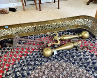 Brass fireplace fender with pierced/filigree design, along with a pair of brass ball-top andirons/fire dogs and additional hearth pieces. Classic decorative fireplace accessories with traditional styling and warm aged patina.