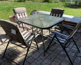 Outdoor table with glass top and four padded chairs.  