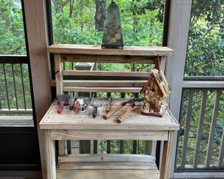 Distressed wood potting bench with shelf, includes garden tools and decorative items.