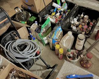 Home and and garden maintenance supplies. Two large black utility bins are filled with various cleaning agents, lawn fertilizers (including Spectracide and Lawn Fertilizer brands), and spray-paints.