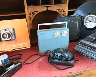 Canon PowerShot A710, Olympus point and shoot,  Pentax binoculars, Panasonic cassette recorder, Vintage RCA Victor transistor radio, Edison record